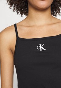 Top senza maniche nero in tessuto morbido con scollo quadrato e logo "cK" bianco sul davanti, posizionato su uno sfondo neutro.