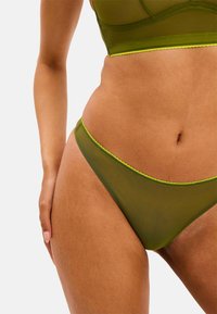 Groene mesh lingerieset met een doorschijnende bh en bijpassende string, verfraaid met neon groene rand. Zachte textuur en aansluitend design.
