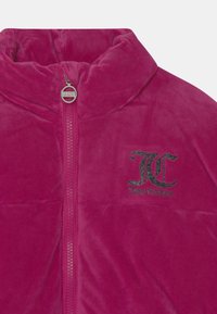 Fuchsiová sametová bunda na zip s vysokým límcem a stříbrným logem na levém prsu. Měkká textura s předním zipem.
