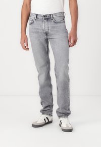 Hellgraue Denim-Jeans mit geradem Schnitt, die eine abgenutzte Textur aufweisen, fünf Taschen und kontrastierende Nähte haben. Getragen mit weißen Sneakers.