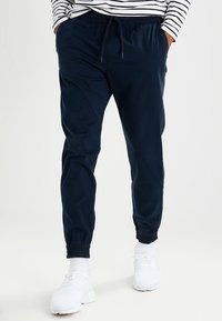 Navy blue jogger pants with elastic cuffs, drawstring waist, and a soft texture, paired with white athletic shoes.