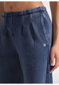 Marinblå sportbyxor med dragsko i midjan, sidofickor, framveck och en liten logotyp på vänster lår. Mjuk, texturerad tyg.