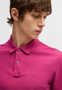 Fuchsiapolo med en texturerad yta, som har en klassisk krage, två knappar och en ton-i-ton "BOSS"-logotyp broderad på bröstet.