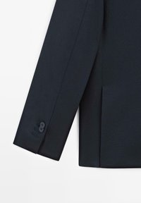 Rękaw ciemnogranatowego blezera o gładkiej fakturze; posiada zapięcie na dwa guziki oraz subtelne detale przeszyć w pobliżu mankietu.