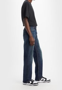 Mörkblå denimjeans med avslappnad passform, kombinerat med en svart t-shirt med kort ärm och svart-vita sneakers.