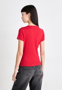 Camiseta de algodón roja con mangas cortas y cuello redondo, de diseño ajustado. Combinada con jeans de pierna ancha gris oscuro, con bolsillos traseros.