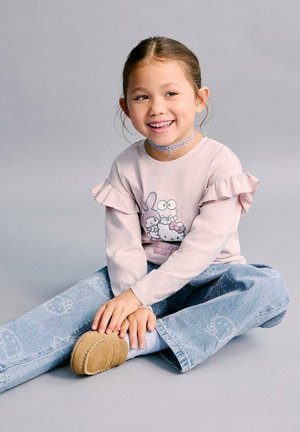 Cămașă roz deschis cu mâneci lungi și volane, cu imprimeu de desene animate, asortată cu blugi largi bleu deschis și papuci bej.