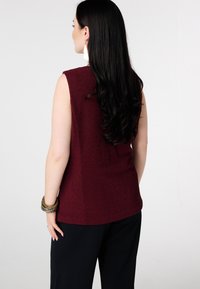 Bordeauxrode mouwloze top met een gestructureerde afwerking, voorzien van een afgeronde zoom en een ontspannen pasvorm, gecombineerd met losse zwarte broek.