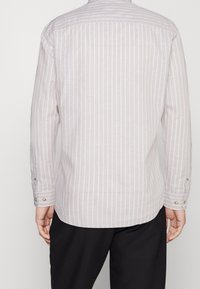 Helle beigefarbene Langarmbluse mit dünnen weißen Streifen, geknöpften Manschetten und abgerundetem Saum. Hergestellt aus einem atmungsaktiven Stoff.