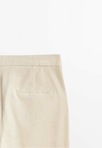 Pantalon en velours côtelé beige montrant la ceinture arrière et une poche passepoilée unique sur le côté droit.