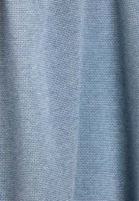 Textielmateriaal in een lichtblauwe kleur met een fijne, gestructureerde weving. De oppervlakte toont een subtiele textuur en een consistent patroon.