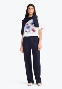 T-shirt blanc avec imprimé floral en rose et bleu, associé à un pantalon large marine, et une écharpe marine drapée sur les épaules.