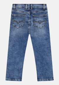 Modré džínové kalhoty s dvěma zadními kapsami, vybledlým a nošeným vzhledem, se malým trojúhelníkovým logem Guess na pravé kapse.