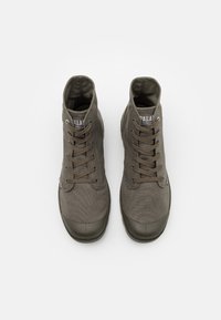 Zapatillas altas de lona verde oliva con puntera redonda, parte superior texturizada, suelas de goma y cordones marrones. Presentan un logo en la lengüeta.