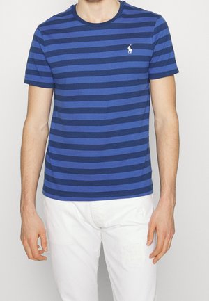 T-shirt à rayures bleues avec des rayures horizontales bleu foncé et bleu clair, col rond, et petit logo blanc sur la poitrine gauche. Matière en coton.