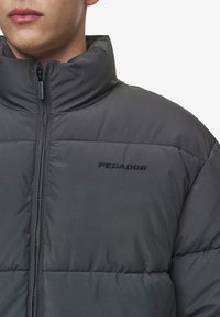 Jachetă puffer gri cu guler înalt, închidere cu fermoar și numele brandului "PEGADOR" brodat pe piept în negru. Panouri texturate vizibile.