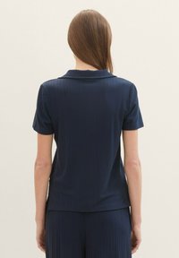 Top de manga corta azul marino con cuello, presentado con rayas verticales y una textura suave, diseñado para un ajuste relajado.