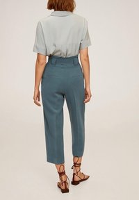 Světle modrá košile s krátkým rukávem a límečkem, zkombinovaná s nohavicemi do pasu v cropped stylu a hnědými sandály na šněrování. Minimalistický design.