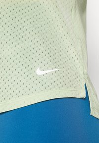 Ljusgrön, ventilerande mesh-atletisk tröja med små hål, med en vit Nike-logga vid fållen, tillsammans med blå leggings.