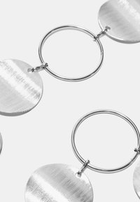 Orecchini a cerchio in argento con pendenti circolari testurizzati con motivi lineari, attaccati a un anello metallico. Design elegante e minimalista.