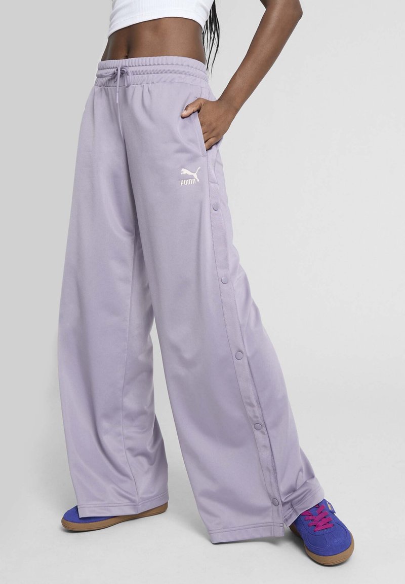 Lilla brede sweatpants med snoreliv, sidelommer og trykknapdetaljer langs ydersiderne. Logo trykt på låret.