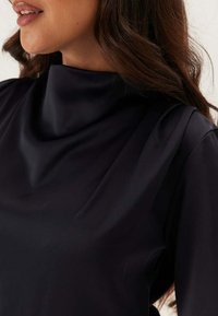 Top blu navy con collo alto, realizzato in tessuto liscio e lucido; vestibilità ampia; si adatta morbidamente alle spalle e al collo; cuciture minime.