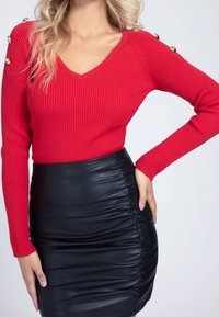 Rød ribstrikket sweater med V-udskæring, med guldknapdetaljer på skuldrene, kombineret med en sort rynket lædernederdel.