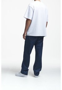Camiseta blanca de manga corta combinada con unos vaqueros oscuros de corte holgado. El conjunto se completa con unas zapatillas de deporte gris claro.