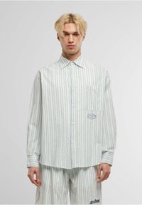 Camisa de manga larga a rayas en azul claro y blanco, con un bolsillo en el pecho y detalle de logo; hecha de una tela suave con cierre de botones.
