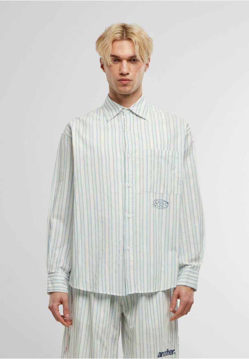 Camisa de manga larga a rayas en azul claro y blanco, con un bolsillo en el pecho y detalle de logo; hecha de una tela suave con cierre de botones.