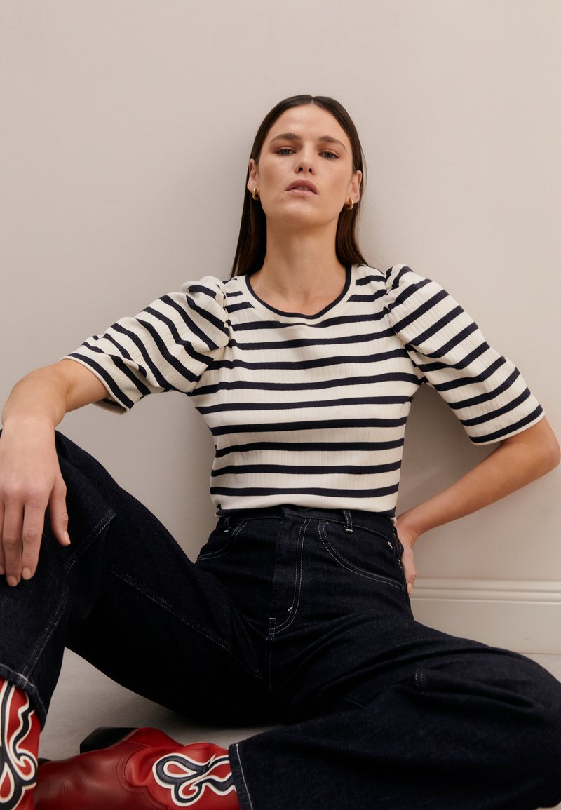 Striped knit top with puff sleeves in cream and navy, paired with dark denim pants and red western-style ankle boots. Simple ribbed texture.