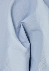 Light blue fabric with a smooth texture, displaying soft folds and subtle sheen. Material appears lightweight and breathable.