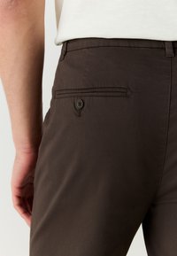 Dark brown trousers featuring a back pocket with a button closure and a straight cut. Material appears smooth and lightweight.