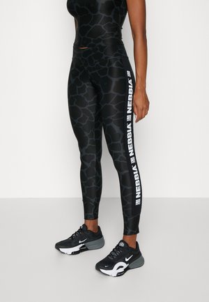 Sorte og grå leggings med et mønster, der ligner dyreskind, med et hvidt logo-stribe på siden og kombineret med sorte træningssko.