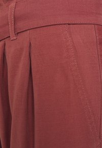 Red cotton trousers featuring a pleated design, visible stitching details, and a textured surface for added depth.
