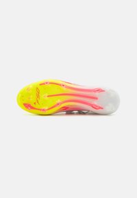 Des chaussures à crampons légères, avec une tige grise, dotées d'une semelle texturée rose et jaune avec des crampons, étiquetées "F50" pour une adhérence sur les surfaces en herbe.