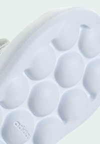 White rubber sneaker sole featuring round textured patterns and embossed "adidas" logo, with a smooth edge transitioning to the sneaker's upper.