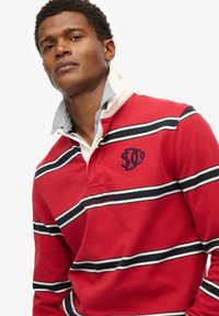 Rødstribet langærmet polo t-shirt med sort og hvid horisontale striber, med en hvid krave og broderet logo på brystet.