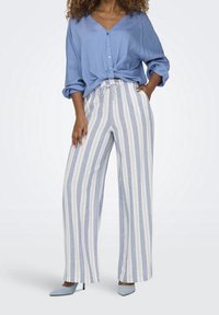 Ljusblå skjorta med uppvikt ärmparad med vida ränder byxor i blått och kräm. Blå spetsiga skor fulländar outfiten.