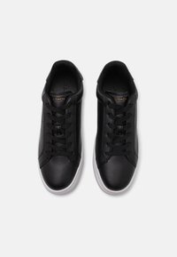 Sneakers din piele neagră cu design cu șireturi, având o textură netedă și tălpi din cauciuc alb. Logo-ul mărcii este vizibil pe lateral.