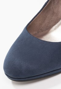 Escarpin en suède bleu avec un bout arrondi, une texture lisse et une doublure intérieure métallique. La chaussure possède un talon bas et plat.