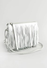 Stříbrná kožená crossbody taška s třásněmi, zipovým uzavřením a tenkým nastavitelným popruhem. Hladká textura a minimalistický design.