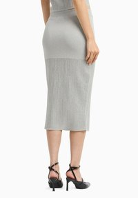 Gonna midi grigia a coste con un design aderente, caratterizzata da una texture liscia e vita alta. Abbinata a scarpe con tacco alto nere a strisce.