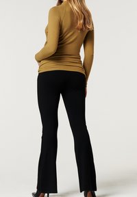 Hnědý dlouhý rukáv s přiléhavým střihem, kombinovaný s černými zvonovými kalhotami. Hladká textura a jednoduchá silueta.