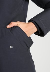 Czarna ocieplana kurtka z boczną kieszenią o gładkiej fakturze i detalem z zatrzaskiem w okolicy nadgarstka.