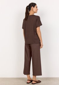 Braun, kurzärmliges Oberteil und weit geschnittene Hose aus weichem Stoff. Das Outfit hat eine lockere Passform, eine glatte Textur und ein einfaches Design.