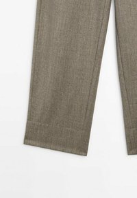 Partie inférieure d'un pantalon en laine marron clair, coupe droite, avec des coutures visibles sur fond blanc.