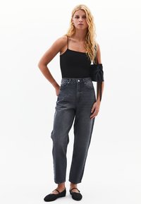 Czarna, gładka koszulka na ramiączkach, szare dżinsy z wysokim stanem w luźnym kroju oraz czarne płaskie buty z paskiem na wierzchu stopy.