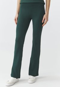 Grüne Schlaghosen aus dehnbarem Stoff. Sie haben eine hohe Taille und seitliche Schlitze am Saum für bessere Luftzirkulation und Stil.