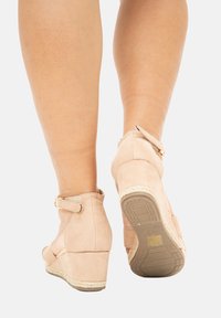 Bottines à talon compensé en suède beige clair avec une lanière et un détail de boucle, semelle texturée et accent en corde autour du talon.